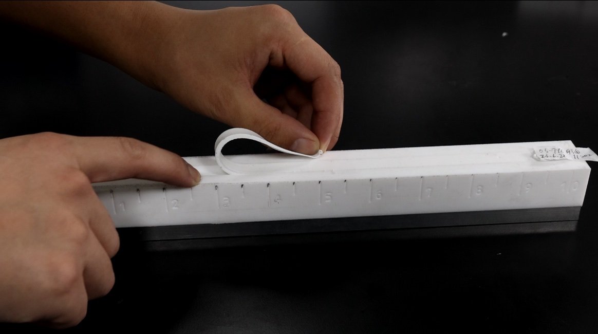 Operator manually observing a cured white sealant strip on a marked fixture