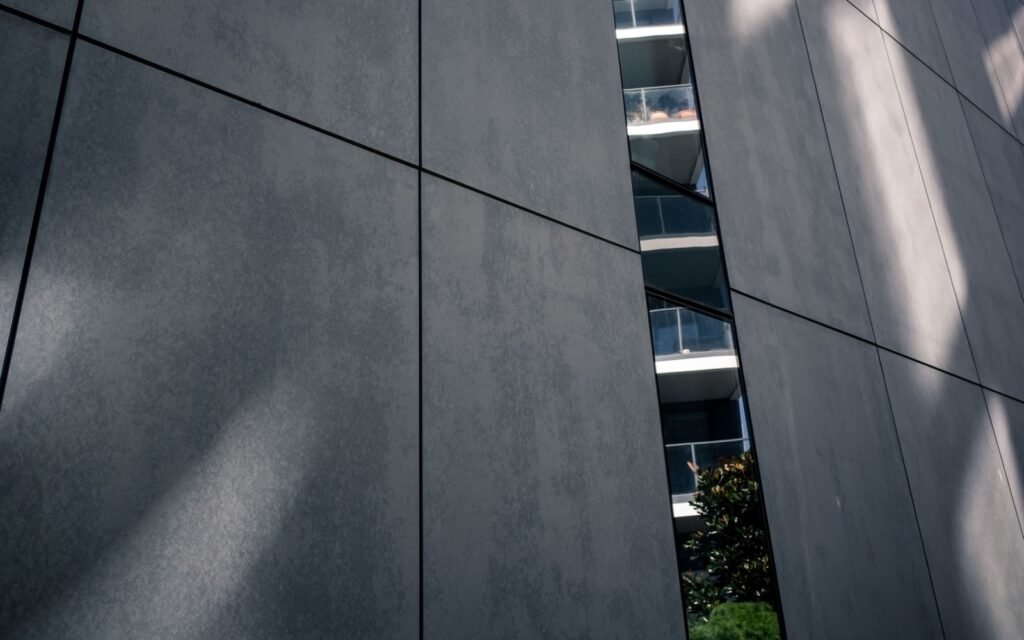 Dark facade panels divided by narrow joints with sunlight across the surface.