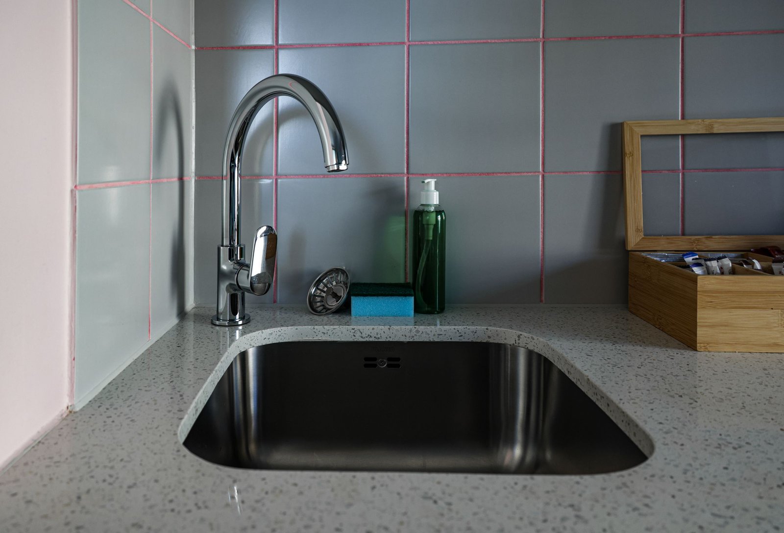 Modern kitchen sink set into a light countertop below a tiled backsplash, with a chrome faucet and soap dispenser.