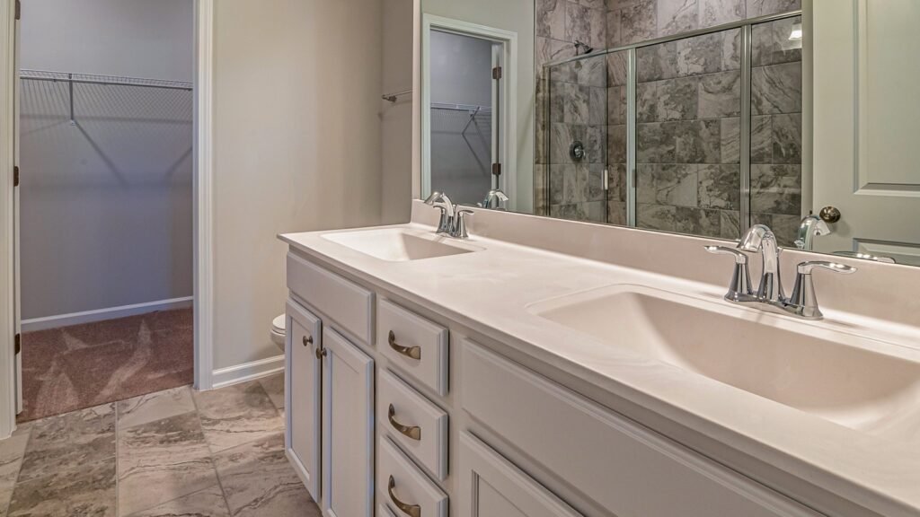 Empty bathroom with dual basins, tiled floor and a glass-enclosed shower.