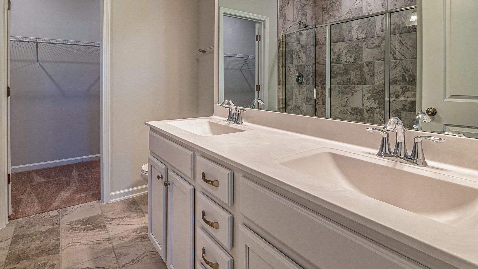 Empty bathroom with dual basins, tiled floor and a glass-enclosed shower.