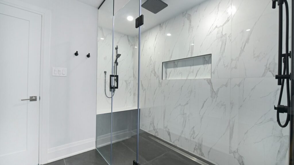 Modern glass-enclosed shower with marble-look walls and dark tiled floor.