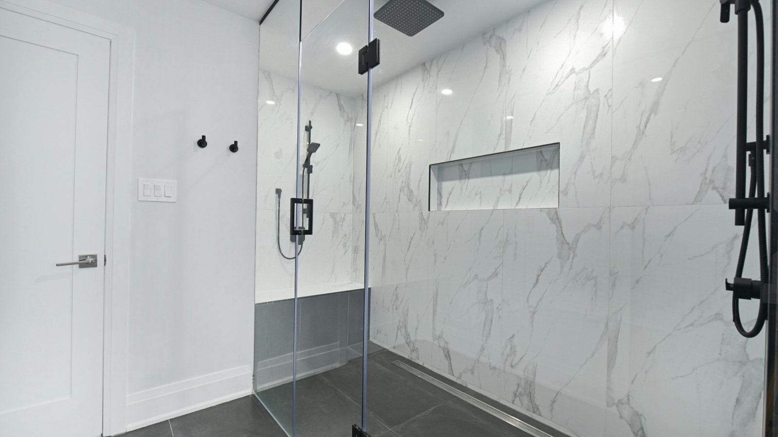 Modern glass-enclosed shower with marble-look walls and dark tiled floor.