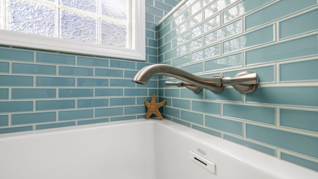 White bathtub meeting blue tiled walls beneath a wall-mounted faucet.