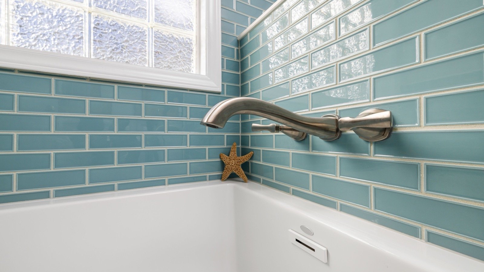 White bathtub meeting blue tiled walls beneath a wall-mounted faucet.