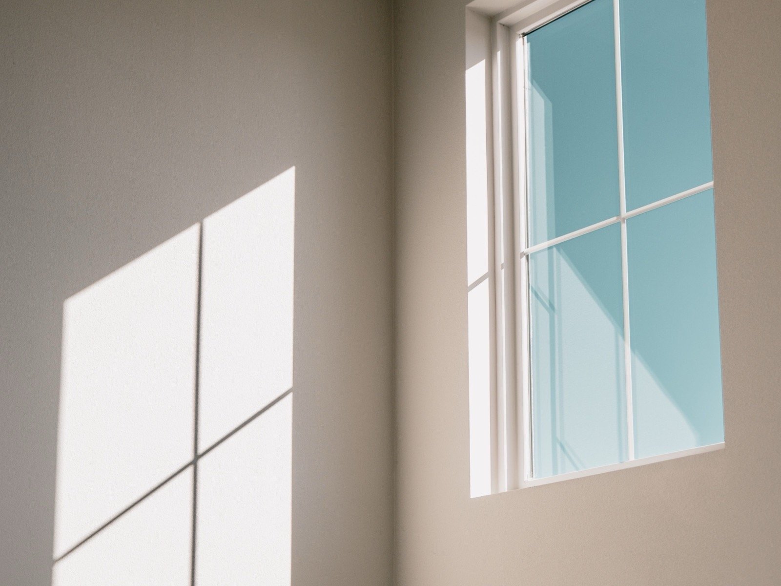 Interior window frame set into a painted wall in direct sunlight.