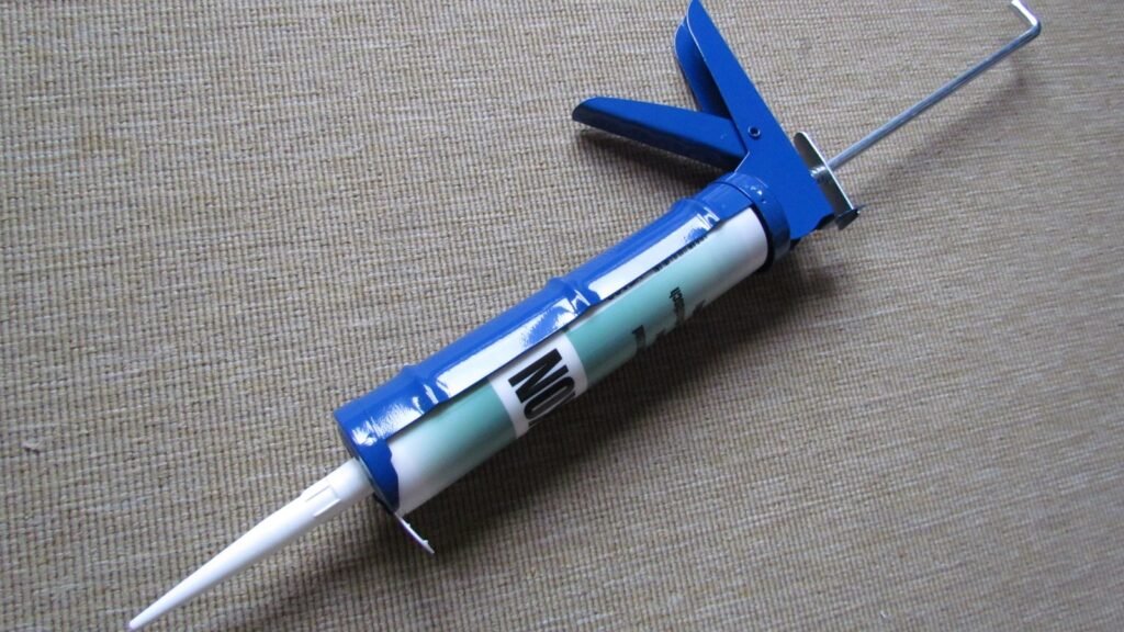 Blue caulking gun holding a sealant cartridge on a gray woven surface.