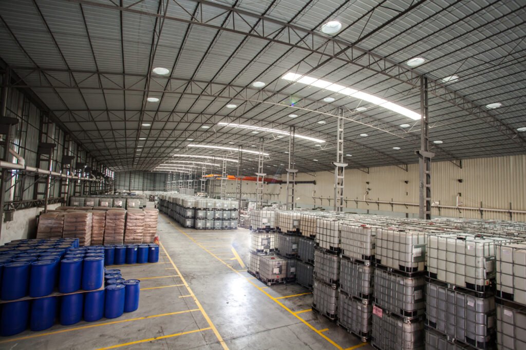 Palletized drums and intermediate bulk containers arranged in a covered factory warehouse for material handling.
