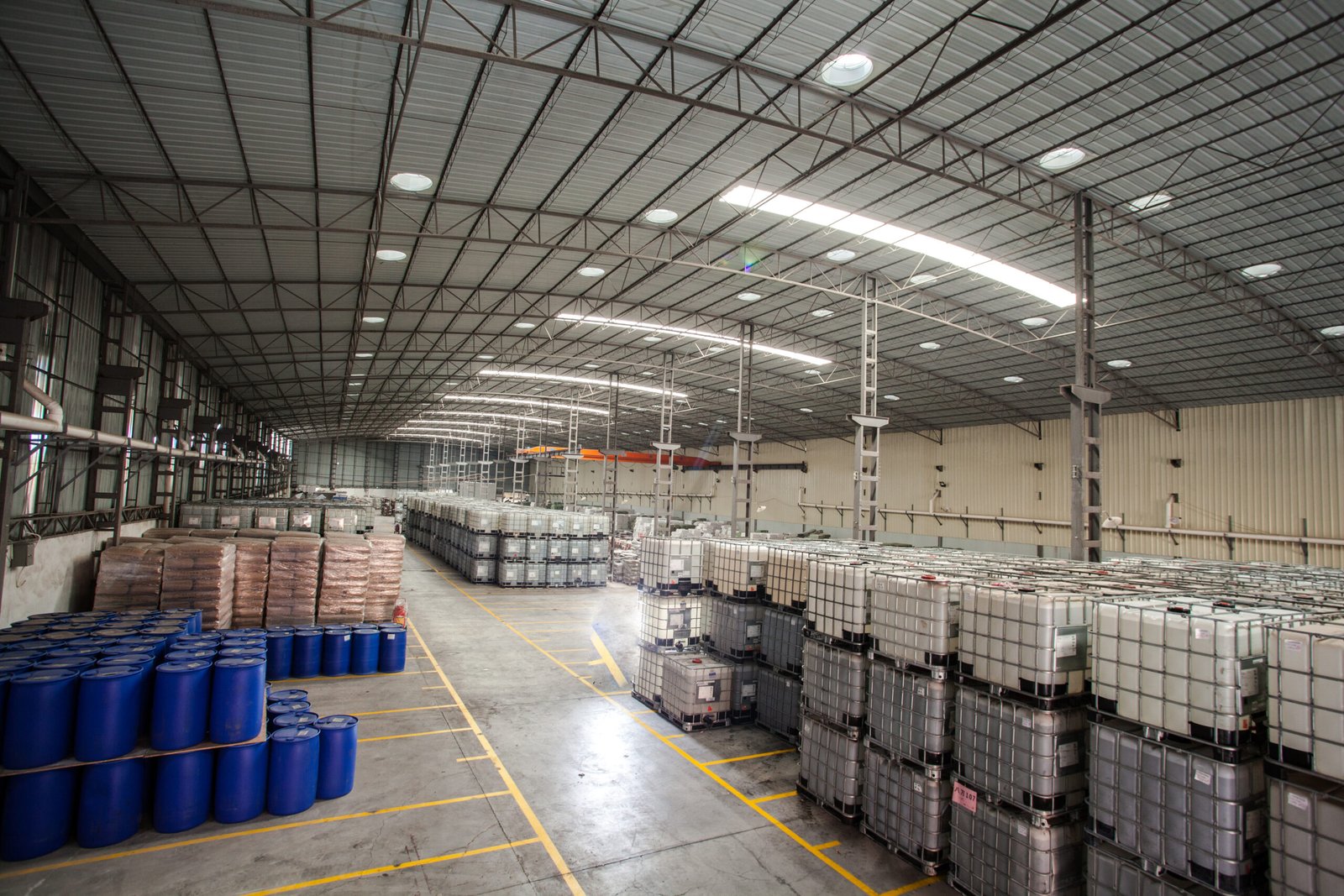 Palletized drums and intermediate bulk containers arranged in a covered factory warehouse for material handling.