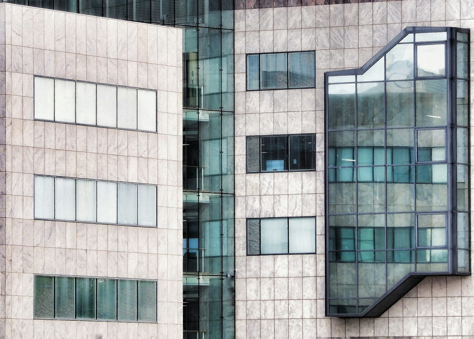 Modern stone-clad facade with reflective glass curtain wall and window panels.