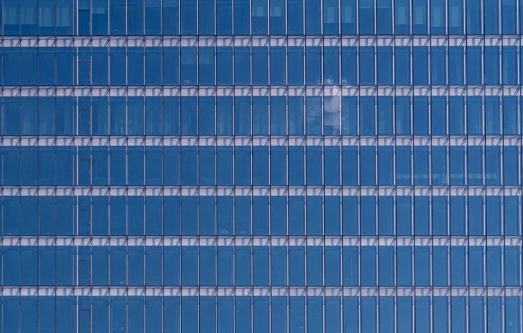 Blue glazed curtain-wall facade with continuous glass panels, fine vertical joints and horizontal floor lines.