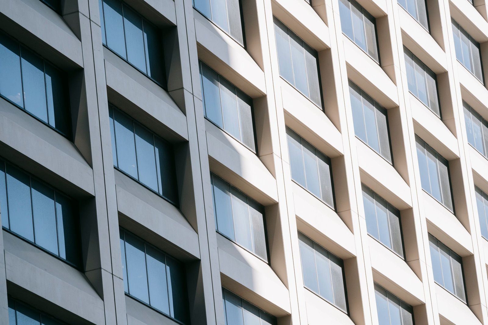 Bright glass-and-concrete facade with repeating windows and angled vertical bays.
