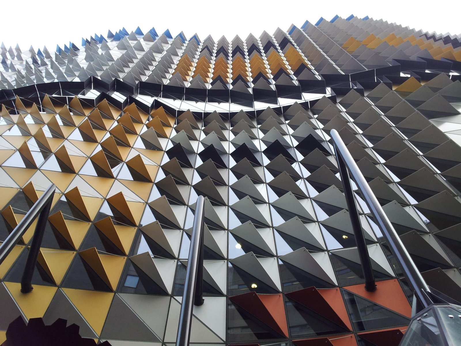 Real building facade with repeated colored aluminum panels in gold, gray, blue and red.