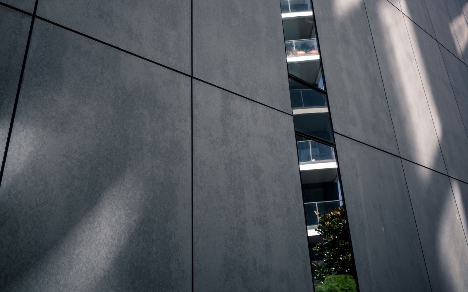 Dark facade panels divided by narrow joints with sunlight across the surface.