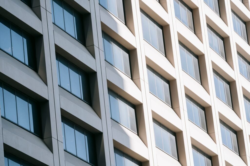 Bright glass-and-concrete facade with repeating windows and angled vertical bays.
