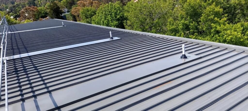 Empty standing-seam metal roof with roof-edge trim and fixed penetrations, viewed across parallel metal panels.