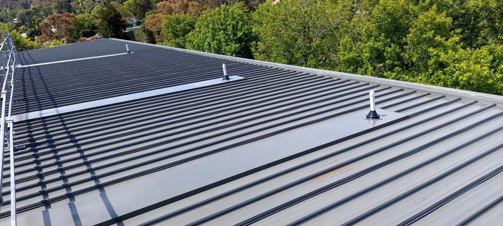 Empty standing-seam metal roof with roof-edge trim and fixed penetrations, viewed across parallel metal panels.