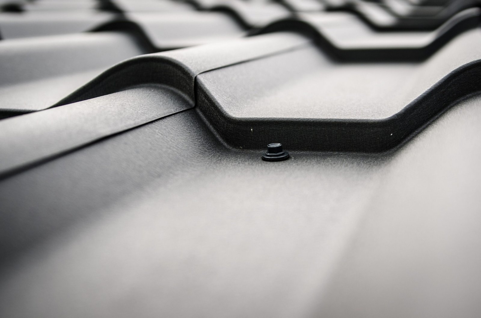Close view of a black steel roof with overlapping raised panels and a fastener.
