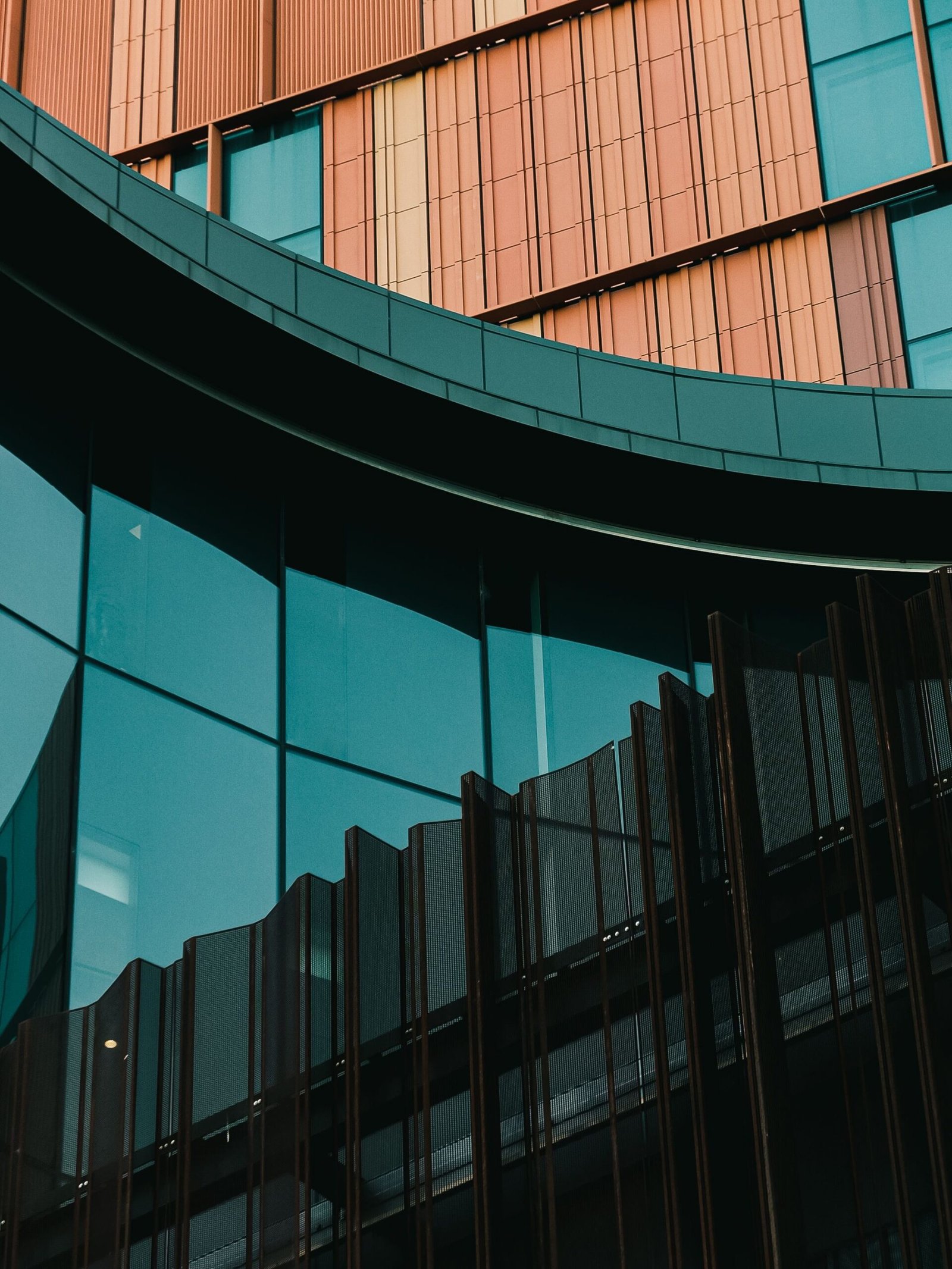 Close architectural facade with teal glazing, curved metal bands and copper-colored vertical panels.