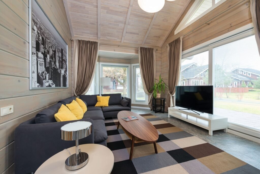 Bright living room with light wood wall and ceiling panels, large windows and a gray sofa.