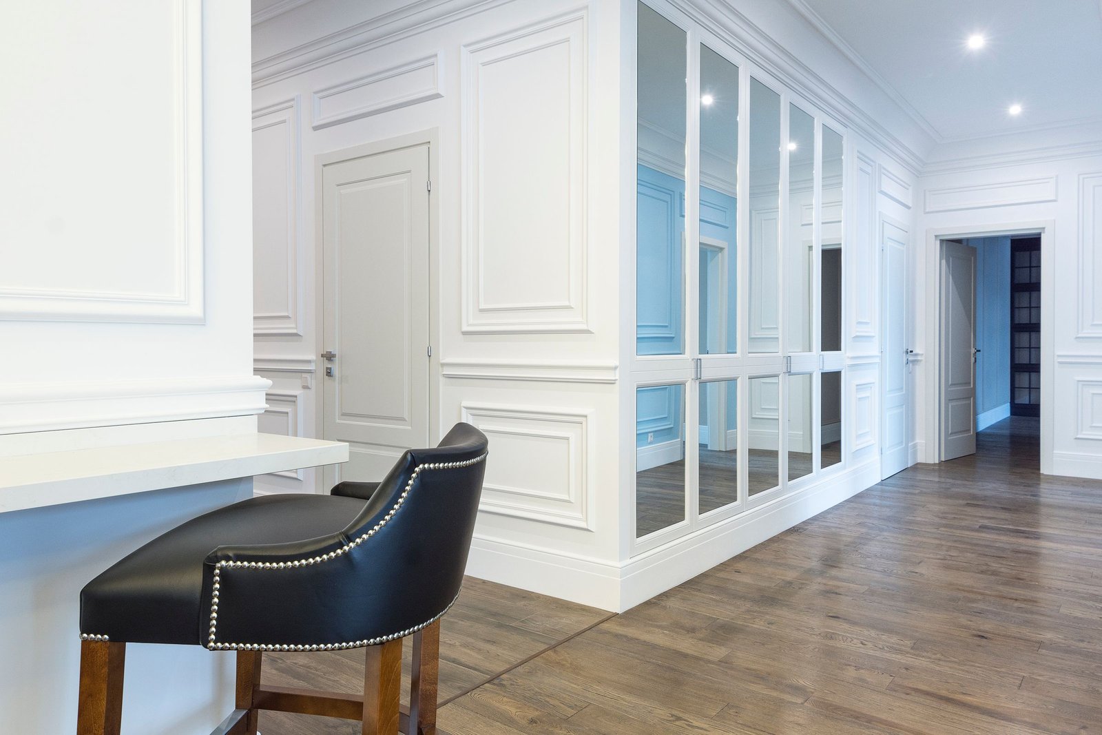 Modern interior with white decorative wall panels, mirrors and wood flooring.