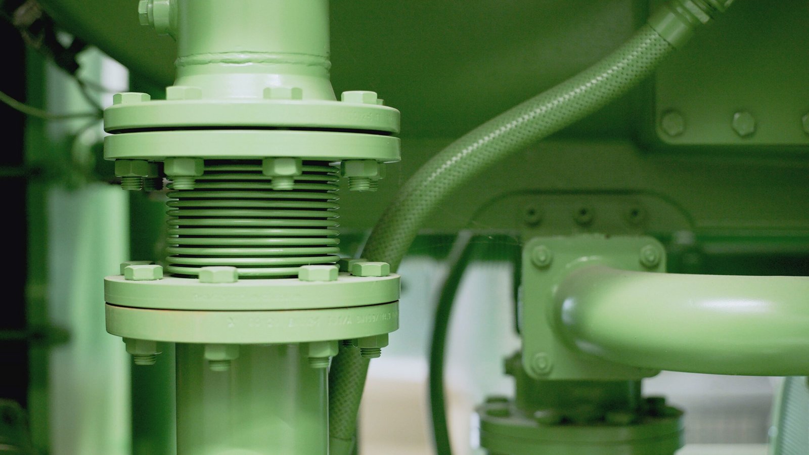 Close view of a green industrial pipe, bolted flange and valve assembly in a mechanical setting.