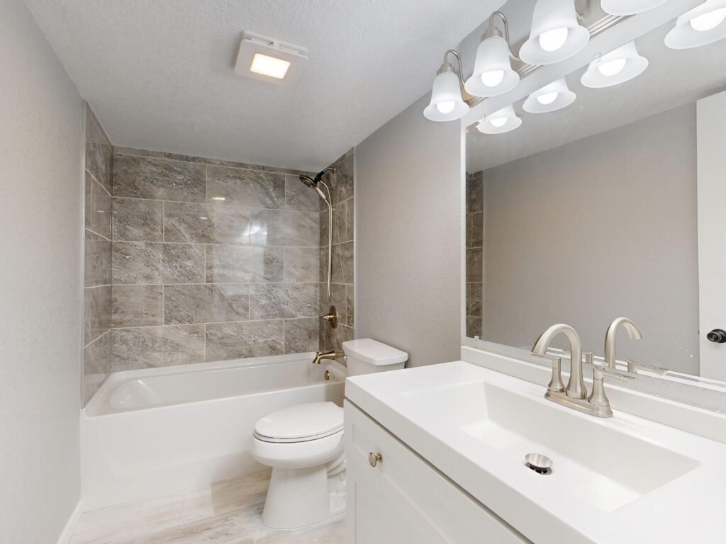 Bright bathroom with a tiled shower, bathtub, toilet and vanity sink.