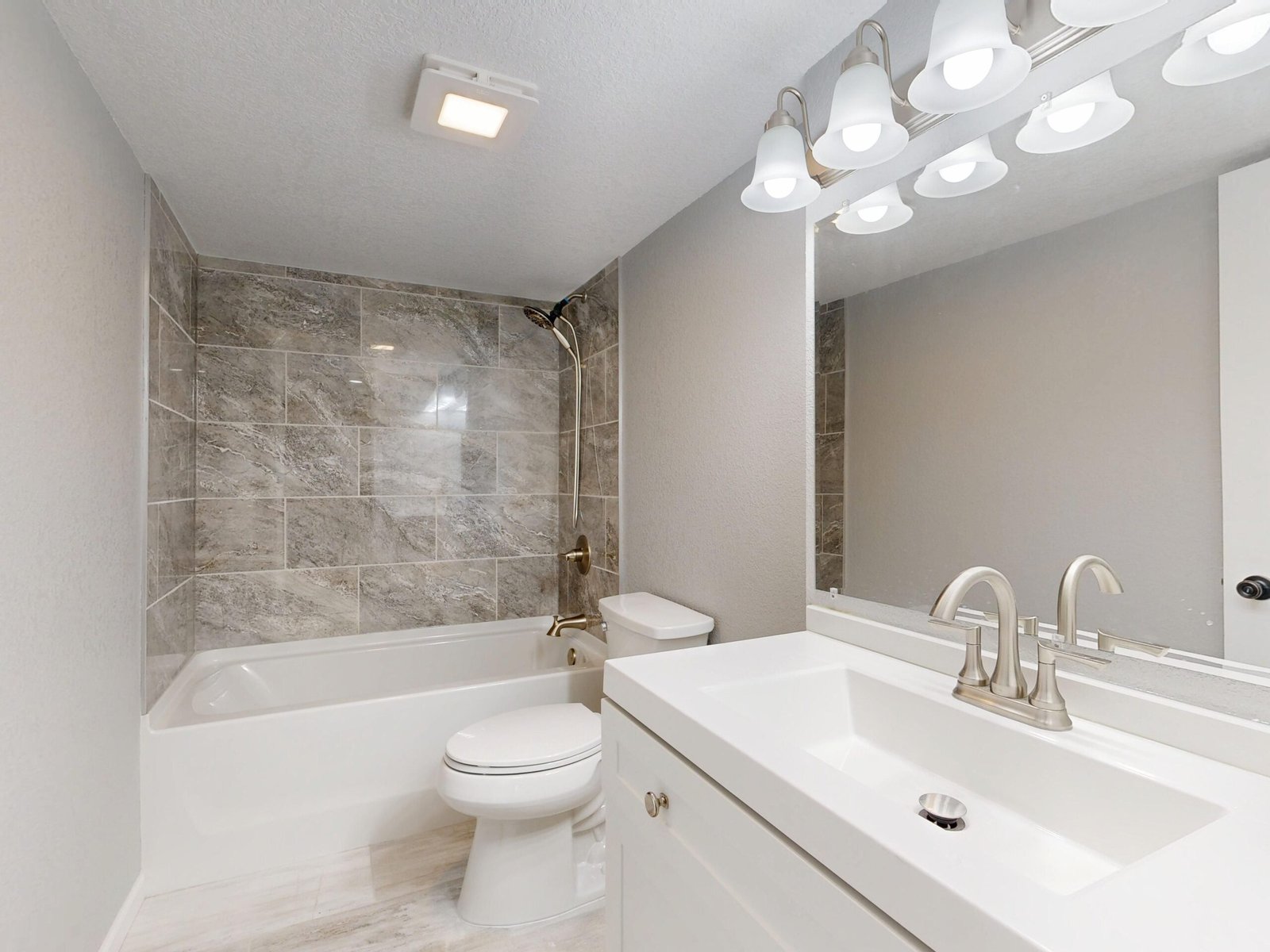 Bright bathroom with a tiled shower, bathtub, toilet and vanity sink.