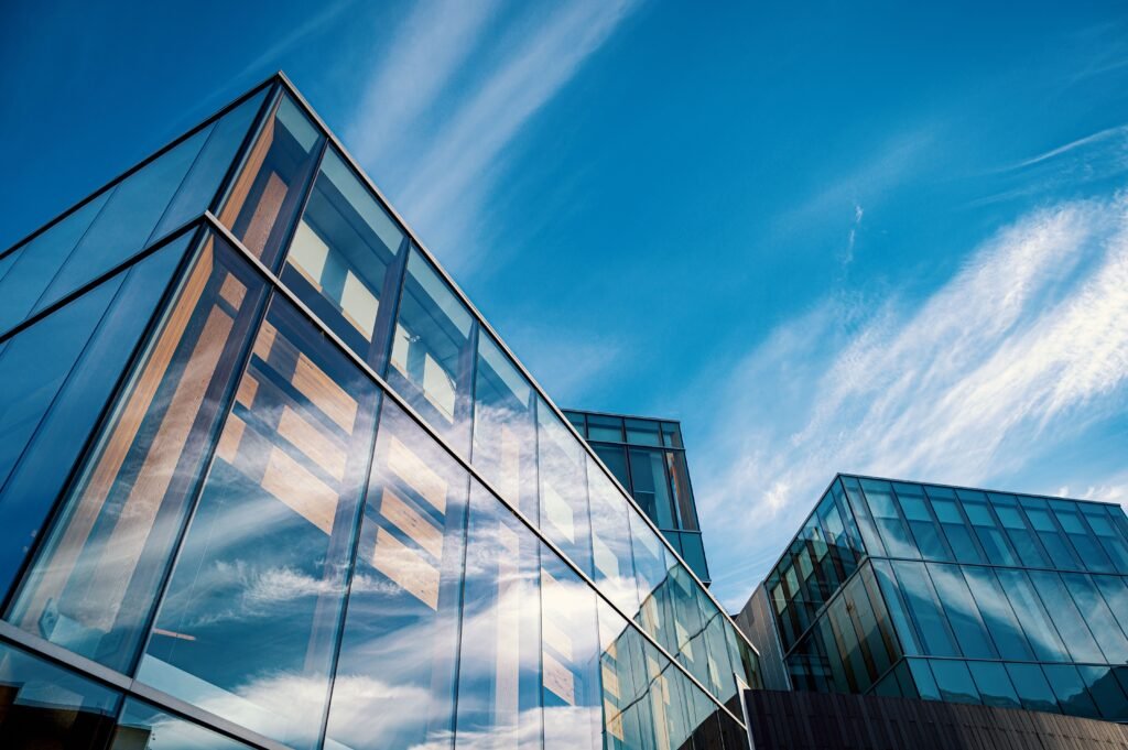 Low-angle view of reflective glass office buildings with dark framing and blue sky.