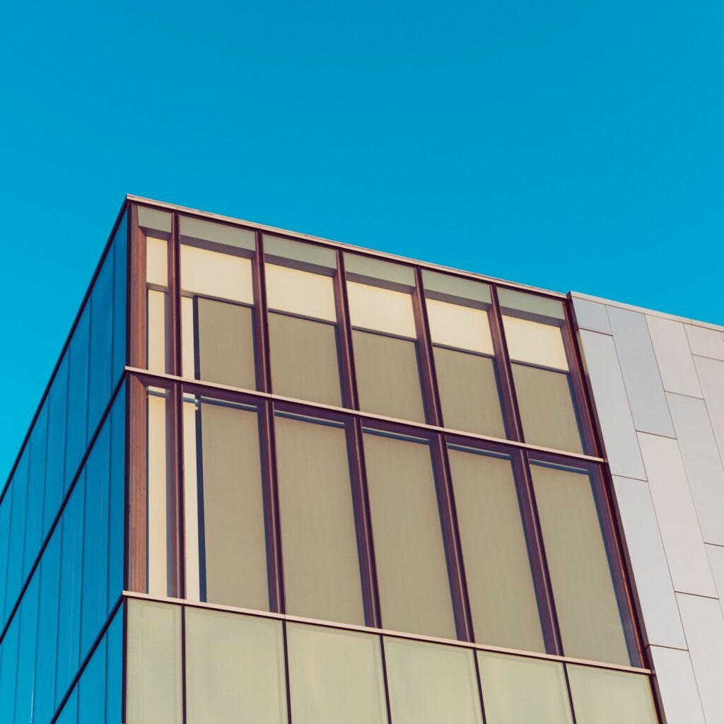 Glass and metal building facade viewed from below against a clear blue sky.