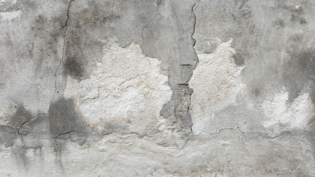 Weathered concrete exterior wall with visible cracking, patching and uneven surface areas.