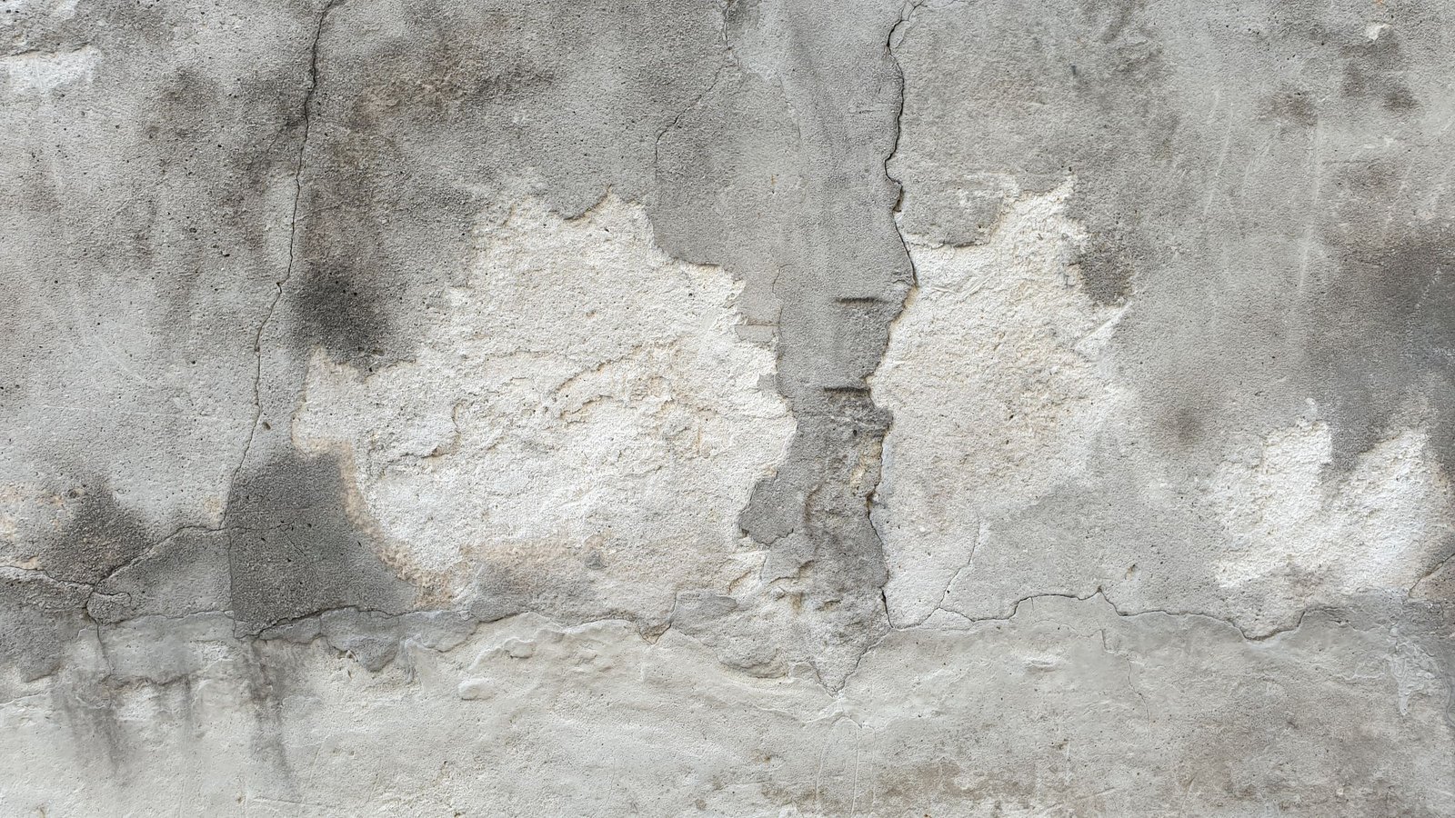 Close view of a weathered exterior wall surface with cracking and uneven patches.