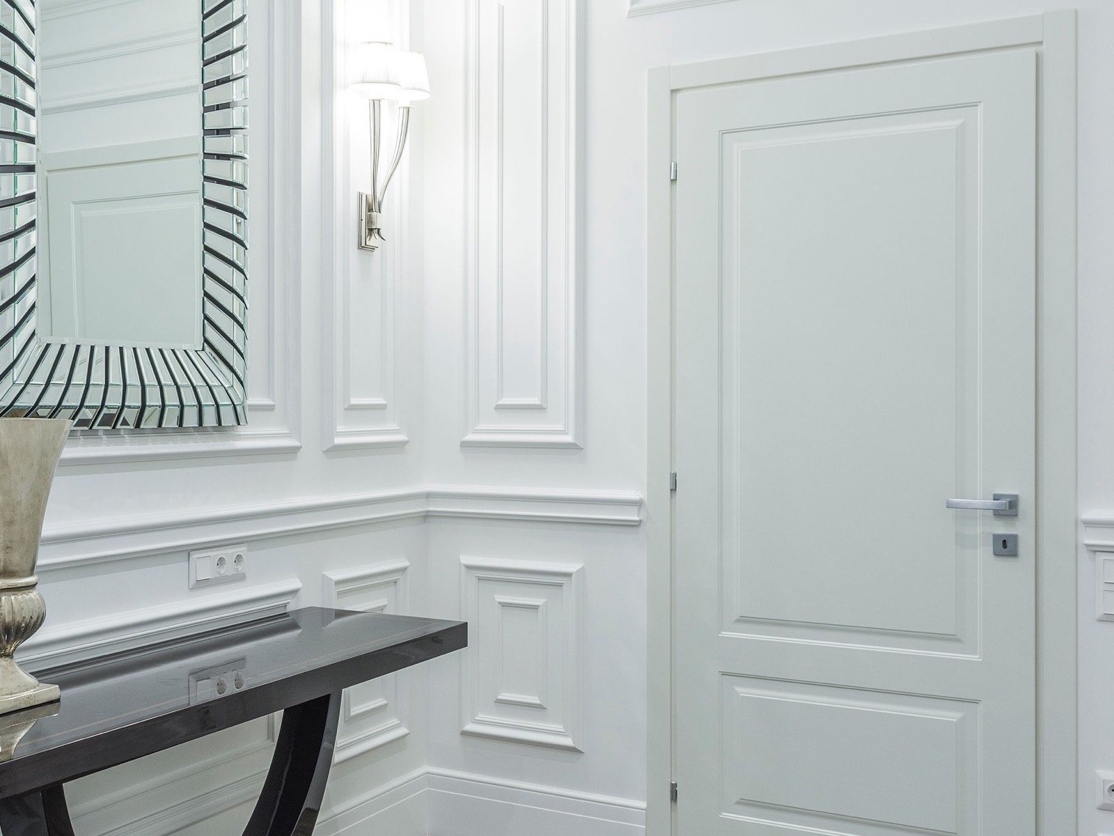 Close interior view of a paneled wall beside a framed mirror and closed door.
