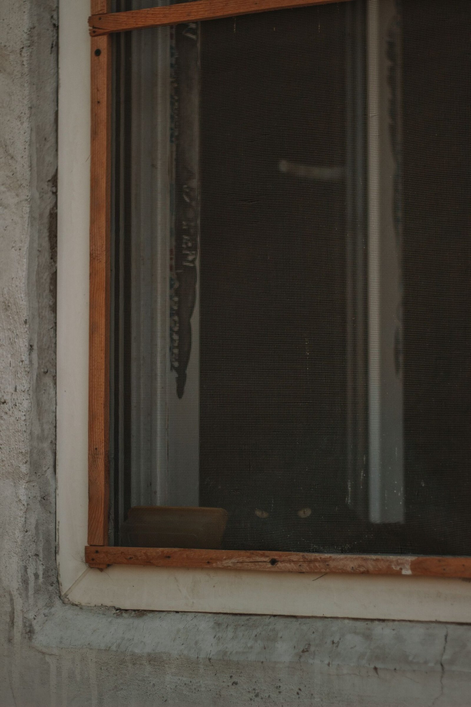 Close view of a wooden window frame beside a screened opening and masonry wall.